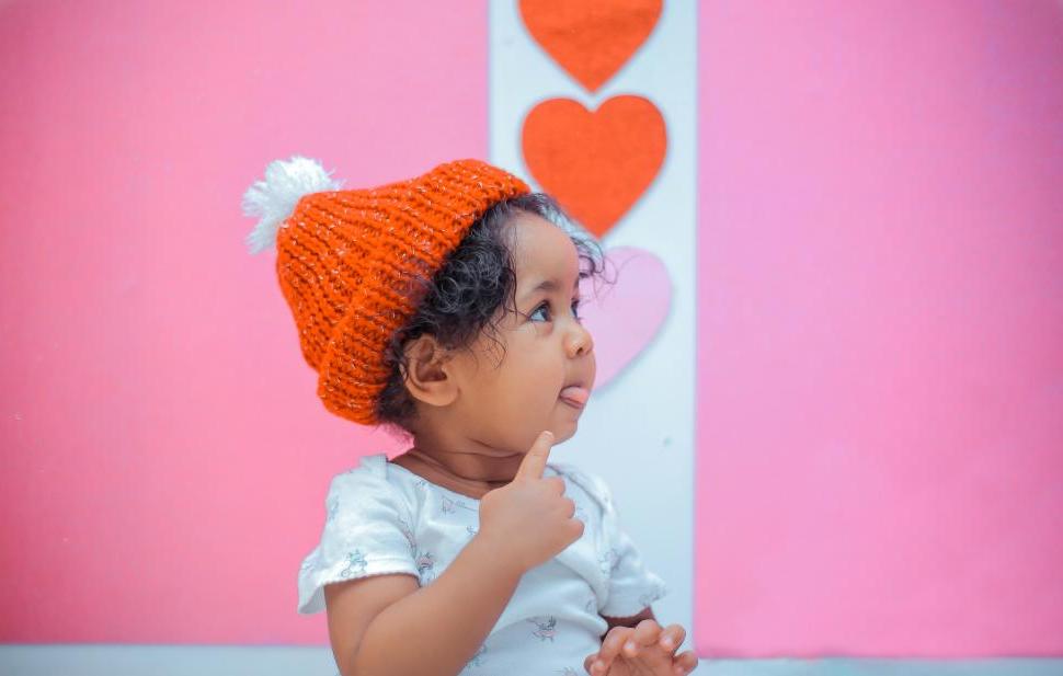 A toddler aged girl sits in front of hearts.