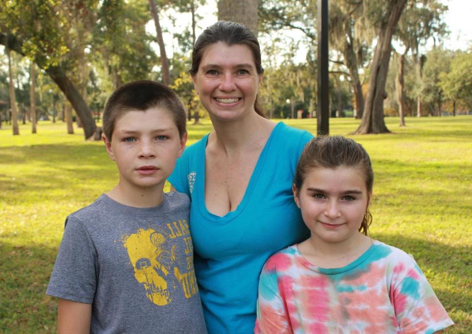 A foster mother stands with a boy and girl in a park.