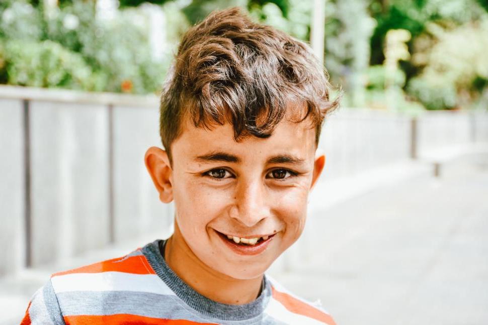 A middle school aged boy in a striped shirt smiles at the camera.