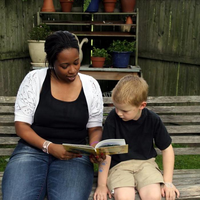 一位非裔美国妇女和一个小孩坐在长椅上看书